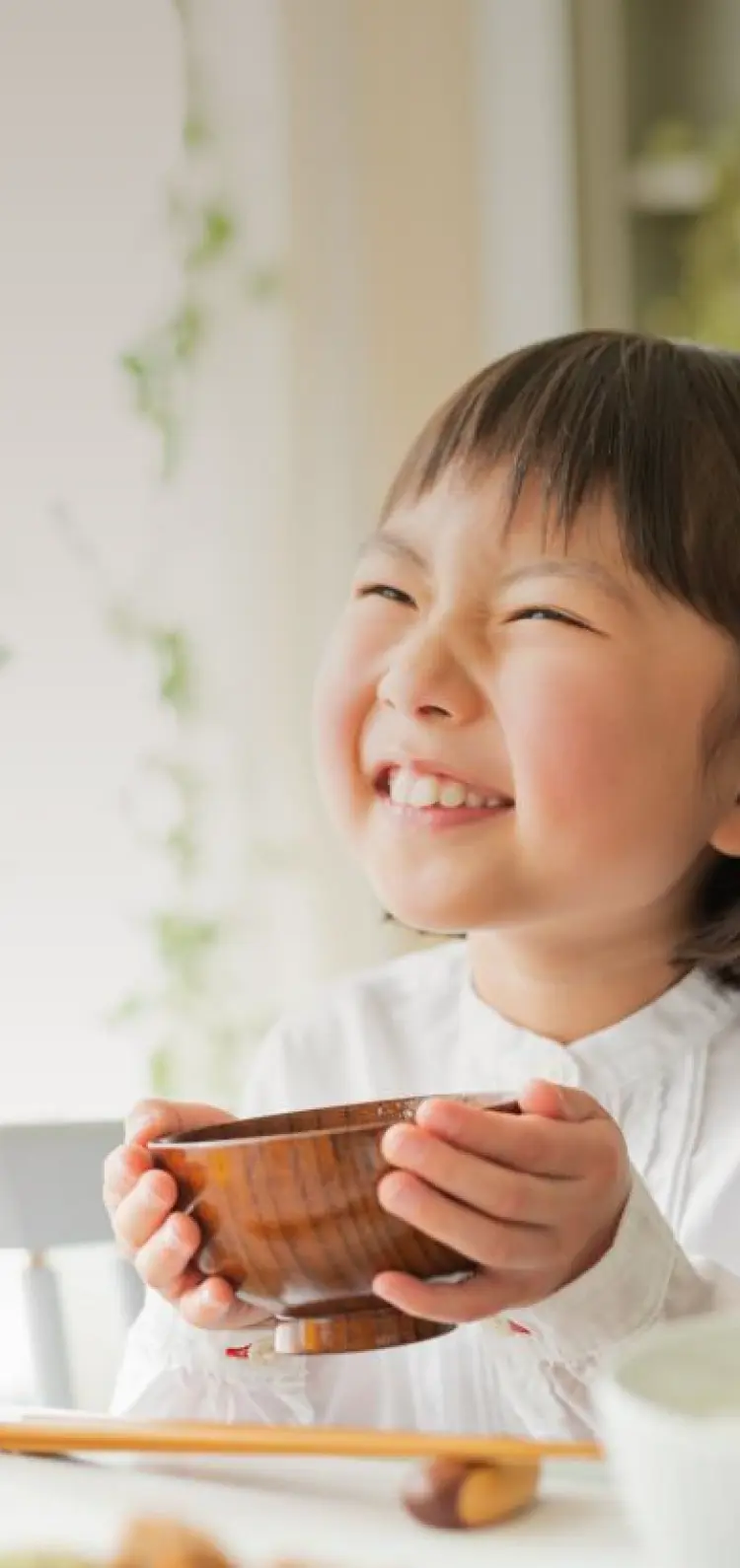 子どもが笑顔でお味噌汁を持っている写真